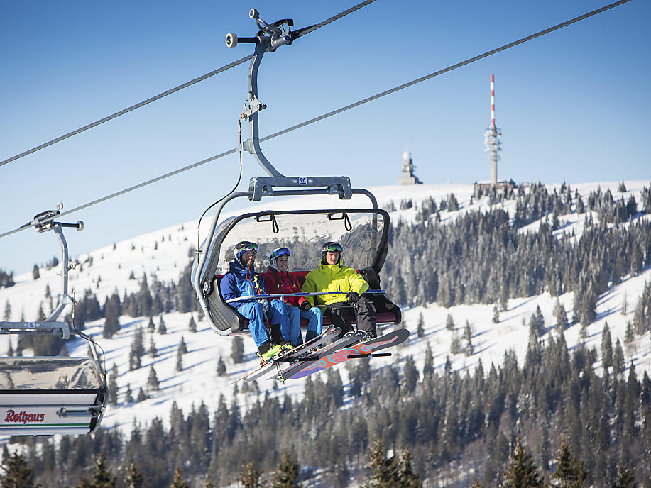 Drei Skifahrer im Sessellift, im Hintergrund der Feldberg